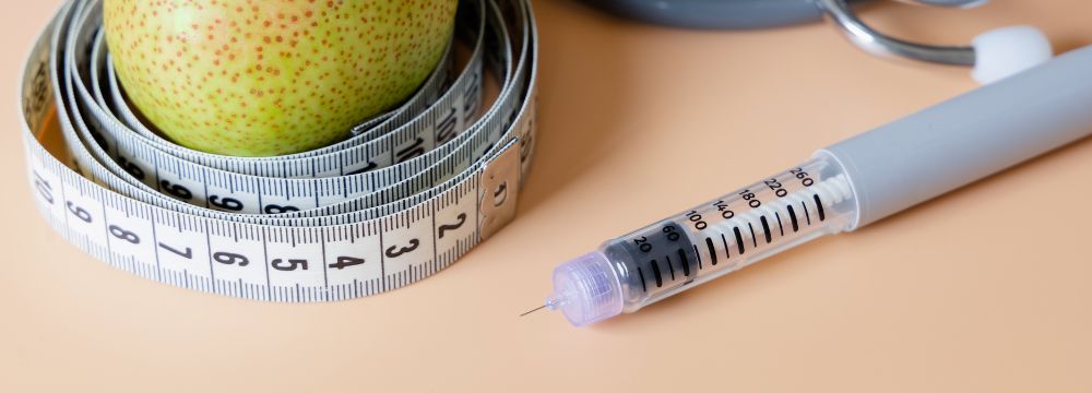 Weight loss medication on peach colored table next to measuring tape and pear 