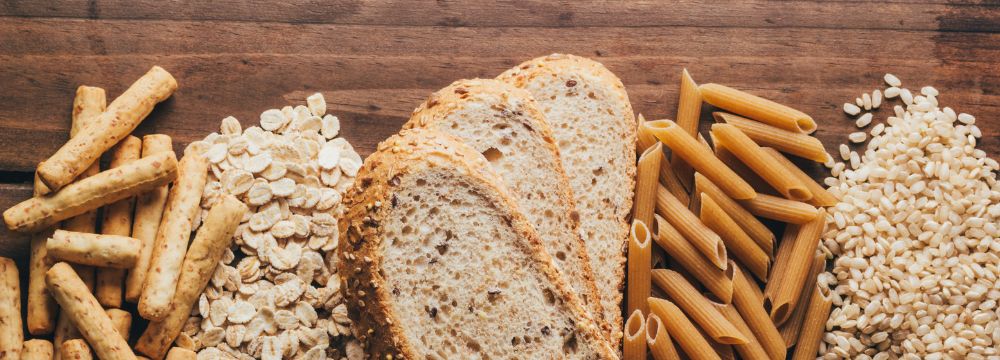 Array of fiber filled foods, pasta, rice, grain, bread, lying next to each other on wooden table 